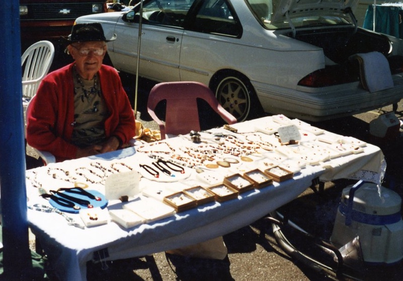 Man sitting behind a table exhibiting necklaces.