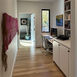 View of hallway desk looking west into Erin's office, where an art piece by Katherine Shaughnessy honors Supreme Court Justice Ruth Bader Ginsburg. The purple mat hanging on the wall was woven on Pentecost Island in Vanuatu.